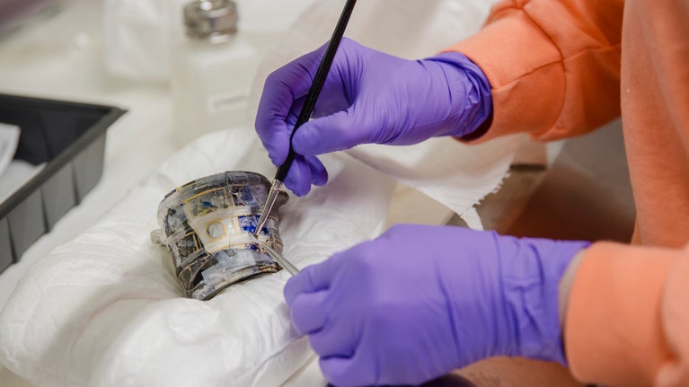 Someone wearing purple gloves holding a tools in both hands as they work on a piece of blue and white ceramic